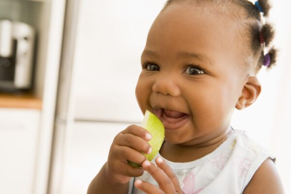 Happy black toddler girl eating apple indoors