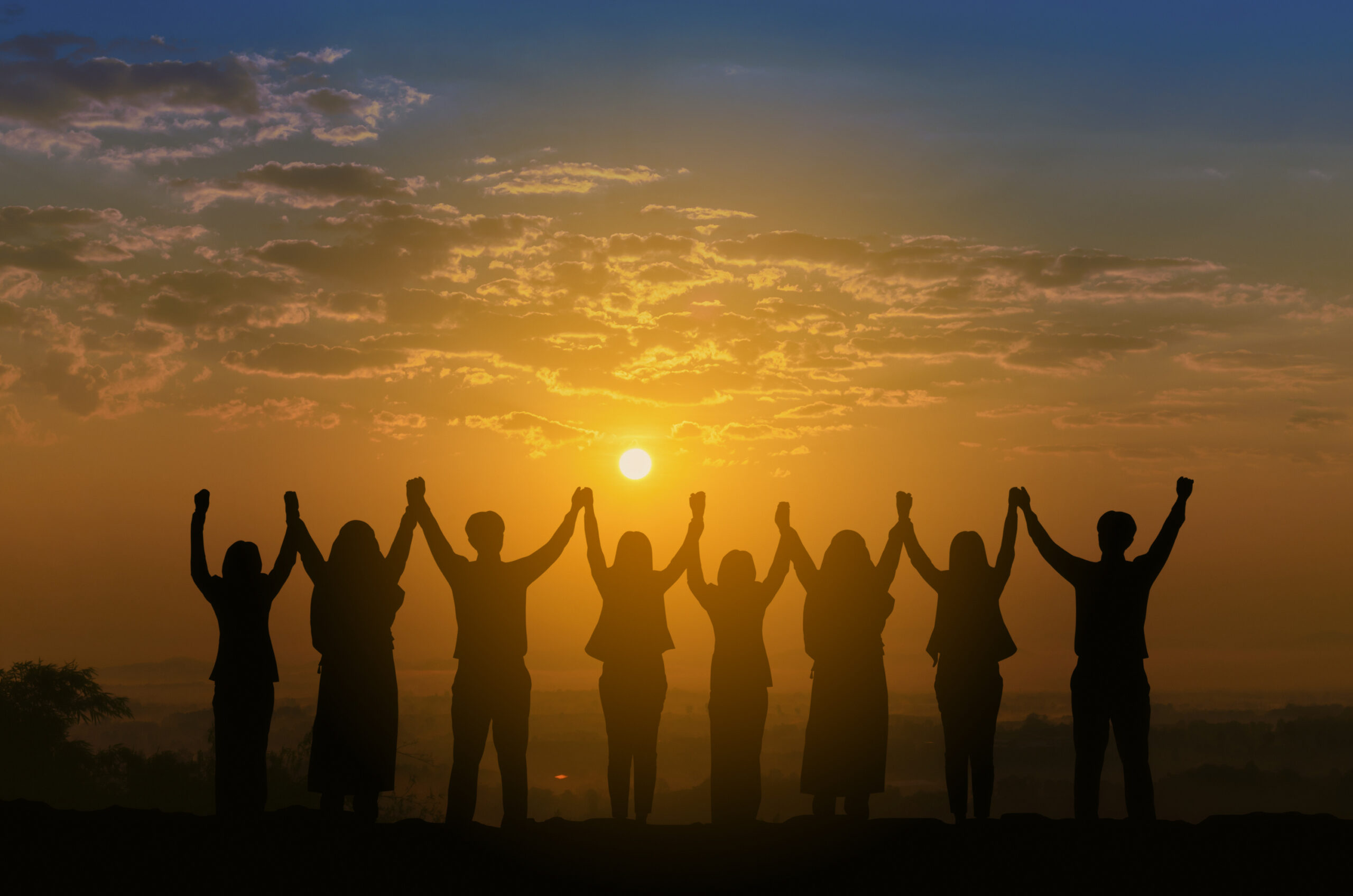 Silhouette of happy teens making high hand over head standing back view on sunrise background,