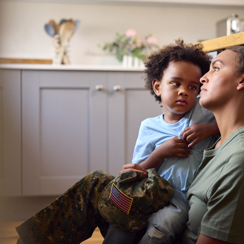 service member parent holds their child, both having looks of concern or stress on their face