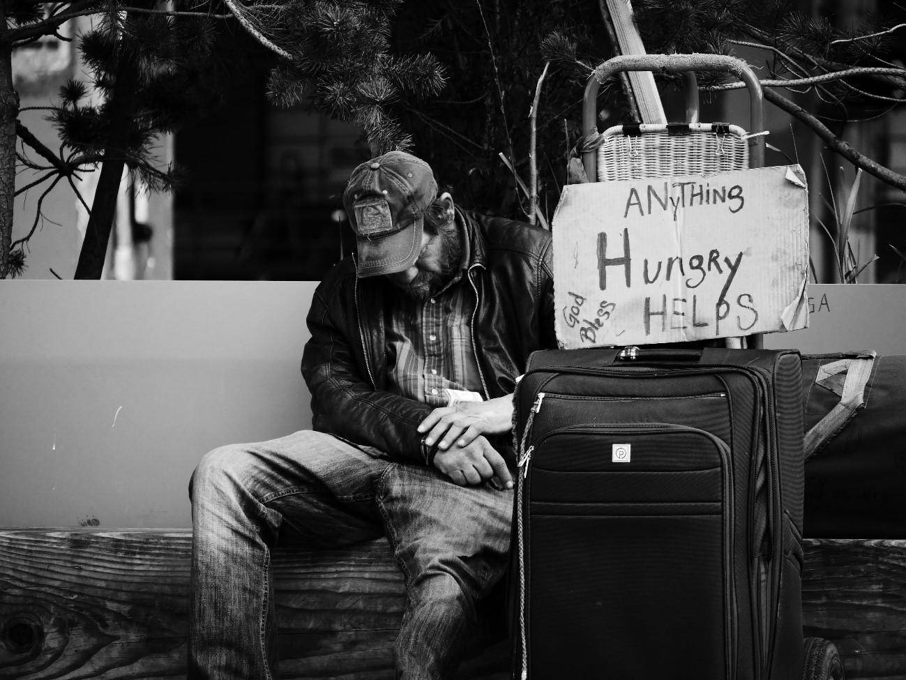 Homeless man sitting in front of a sign that says "Hungry Anything Helps"