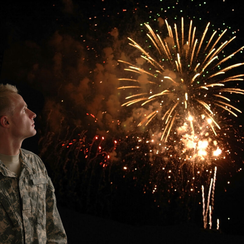 A soldier in combat fatigues looking up at the fireworks