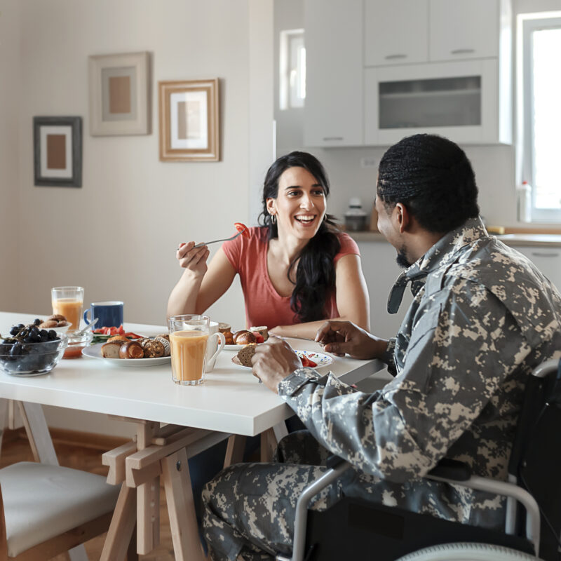 Disabled African American Male Soldier in a Wheelchair In Military Uniform and His Wife Enjoying One Another While Having Breakfast at Home. Homecoming, Reunion, Returning Home to Family. Food, Home, Couple and Happiness Concept