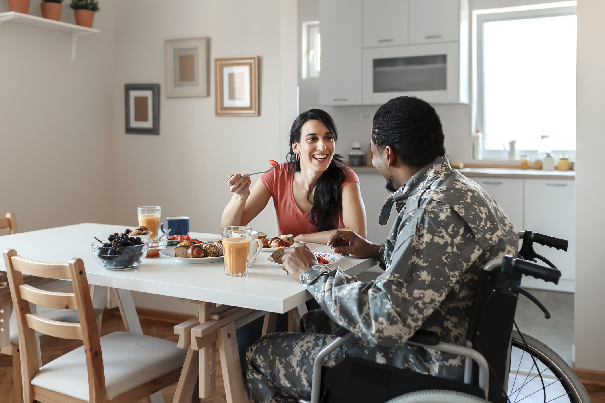 Disabled African American Male Soldier in a Wheelchair In Military Uniform and His Wife Enjoying One Another While Having Breakfast at Home. Homecoming, Reunion, Returning Home to Family. Food, Home, Couple and Happiness Concept