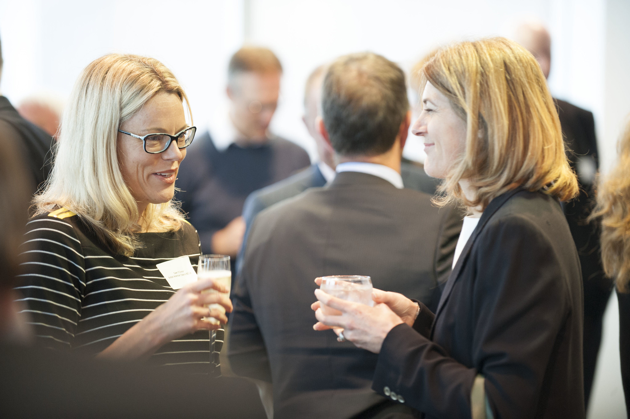 Two women in business attire talk to each other at a networking event.