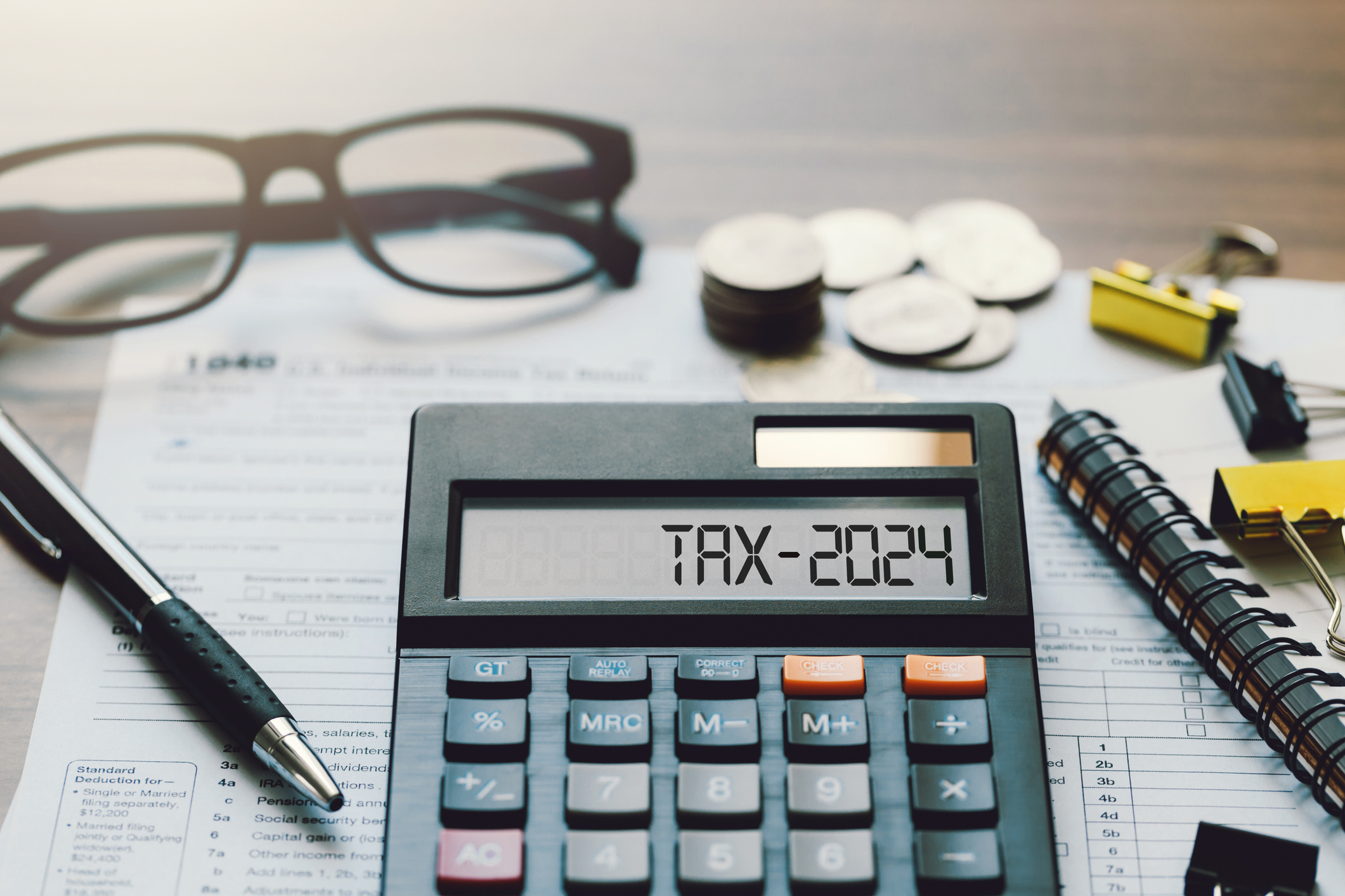 calculator that reads tax-2024 background includes a tax form, glasses, pen and change