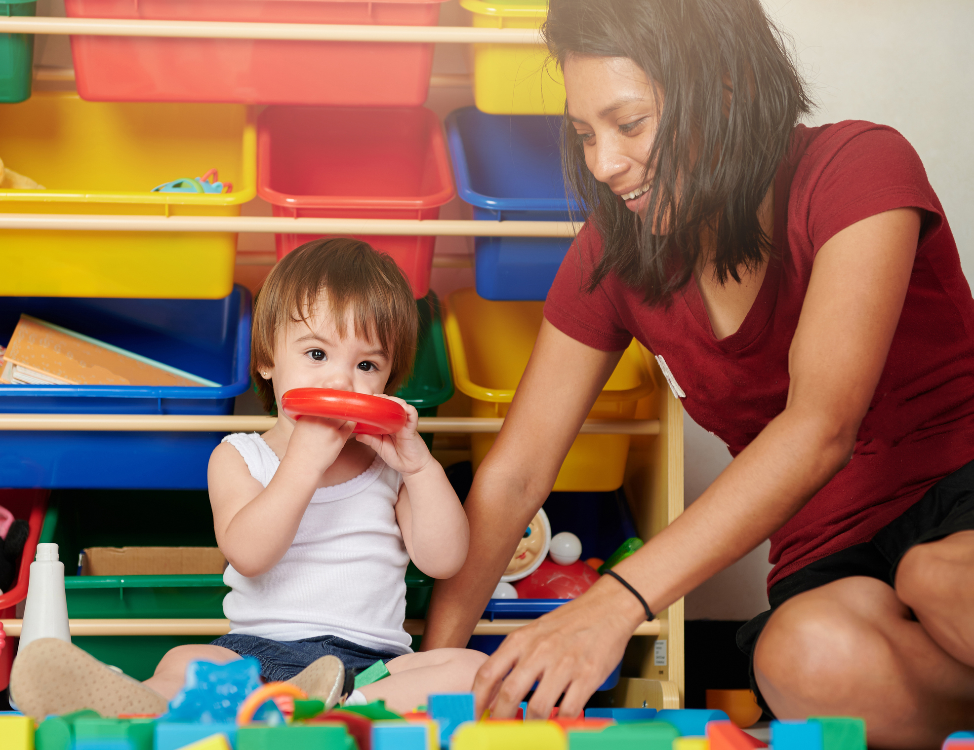 Female child care professional playing with young child and colorful toys.