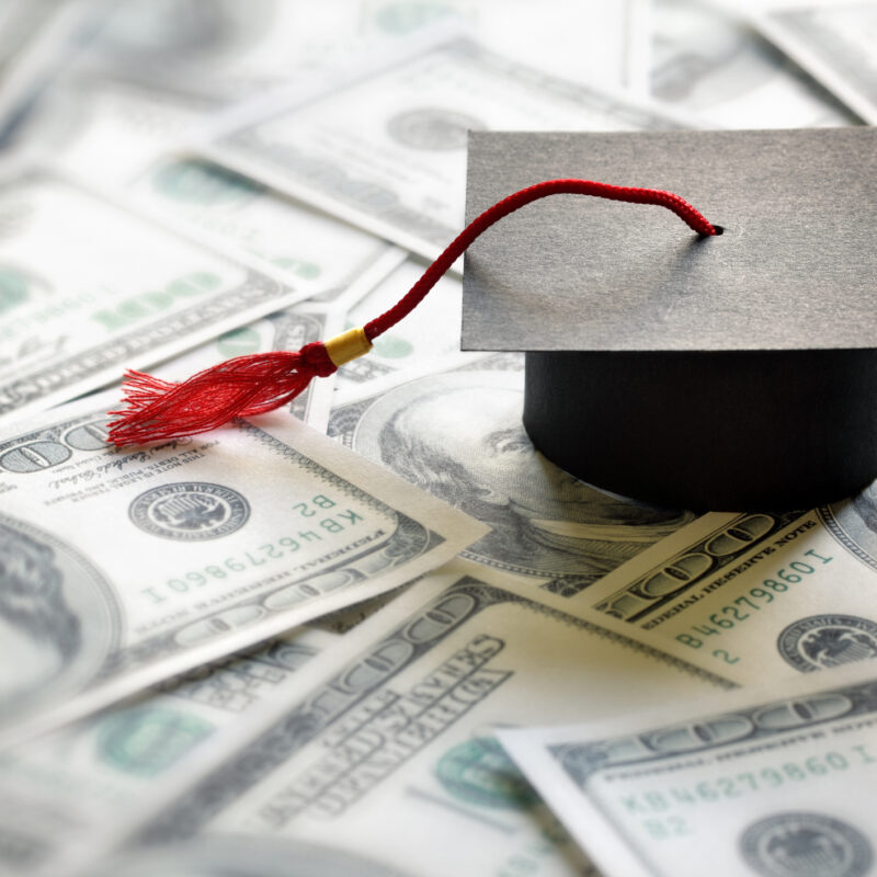 graduation cap on top of one-hundred dollar bills