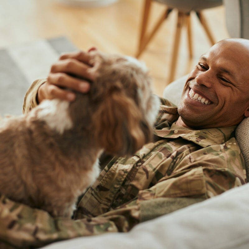 Smiling service member pets dog while laying on the couch.