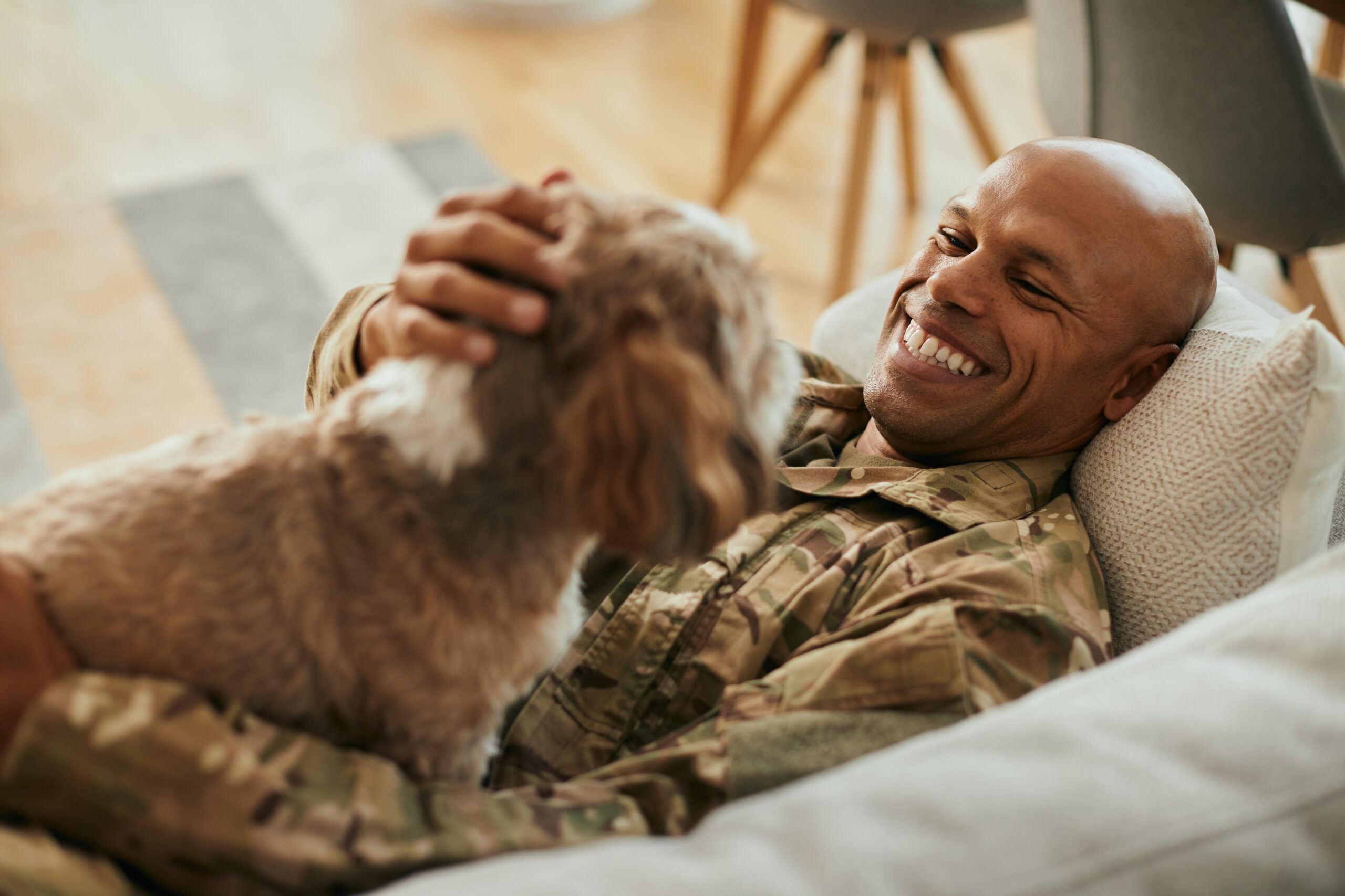Smiling service member pets dog while laying on the couch.