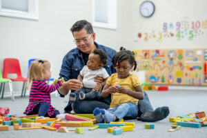 Childcare professional plays with three small children while sitting on the floor.