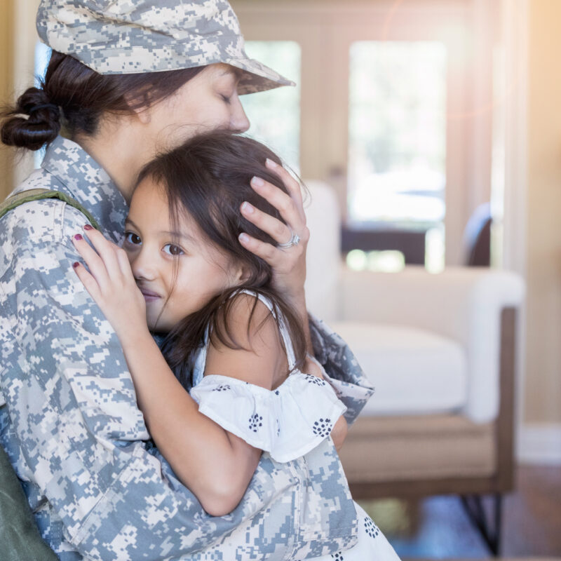 Upset female soldier hugs her little girl goodbye before leaving for long military assignment.