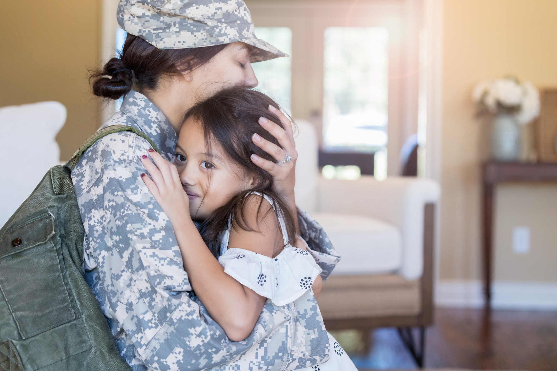 Upset female soldier hugs her little girl goodbye before leaving for long military assignment.