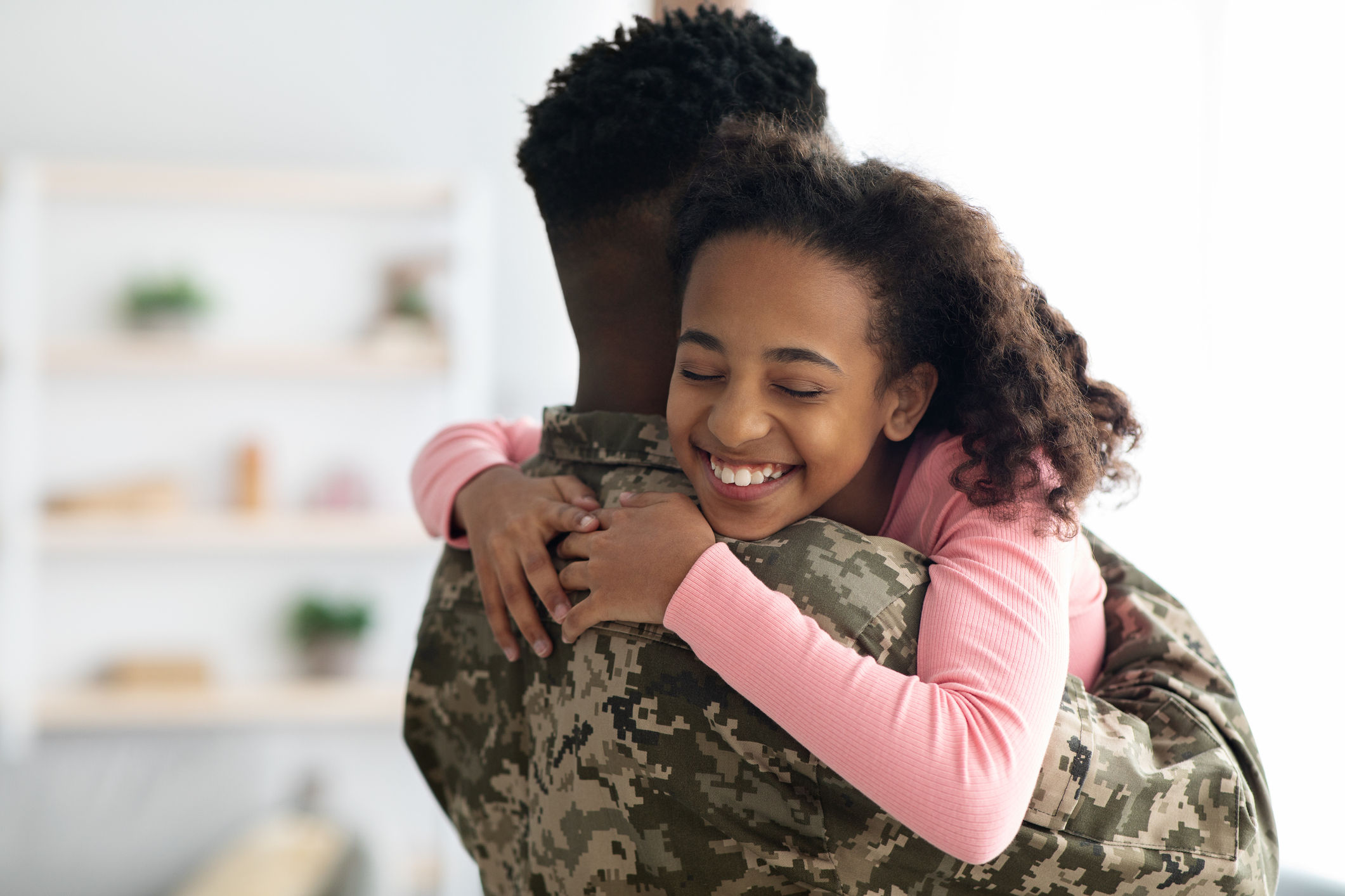 Portrait of happy cute curly african american teen girl hugging her dad soldier and smiling with closed eyes, black man in military uniform return home from army, embracing his daughter