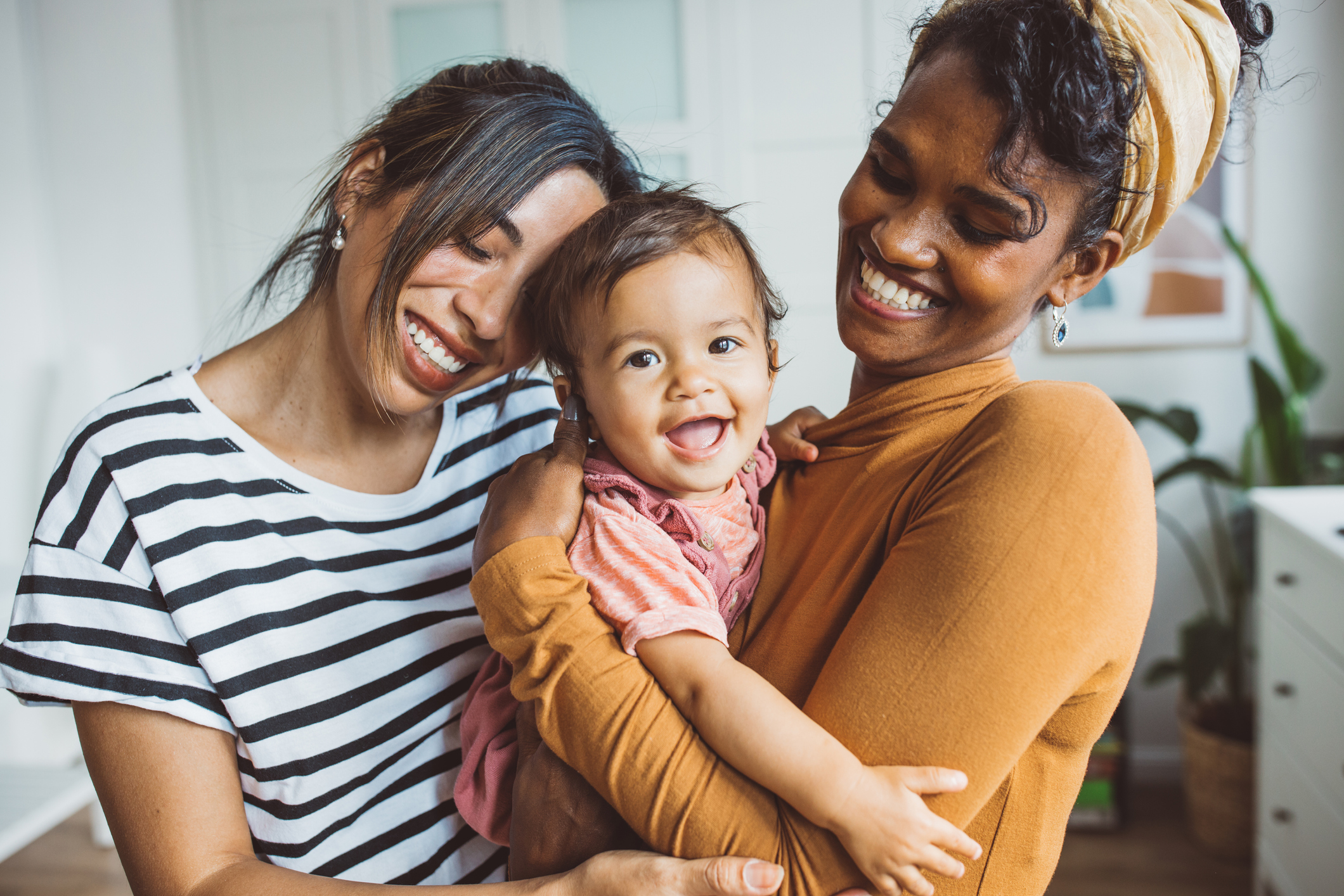 Two smiling black or multiracial women holding a happy baby while all embrace