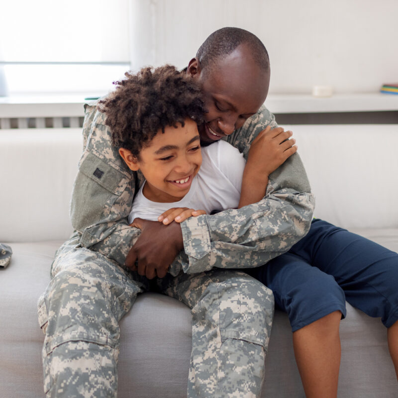 military dad and his son are playing on the sofa at home