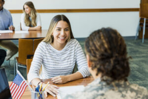 A young adult woman smiles as she listens to the unrecognizable mid adult female recruiter.