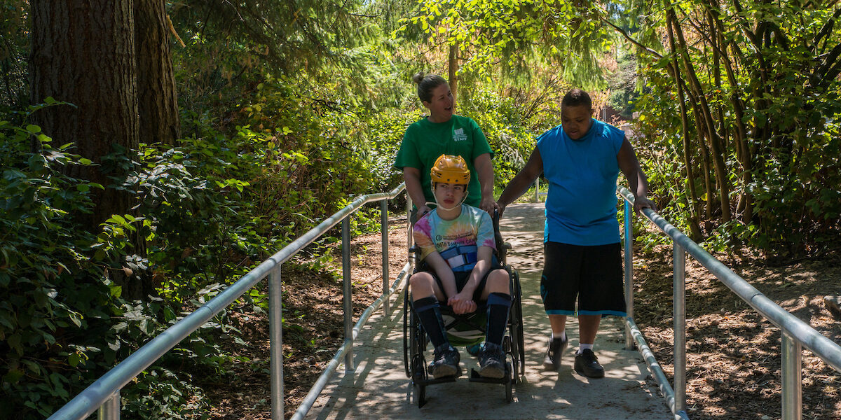 Two teenagers with disabilities and an adult camp counselor walking through the woods