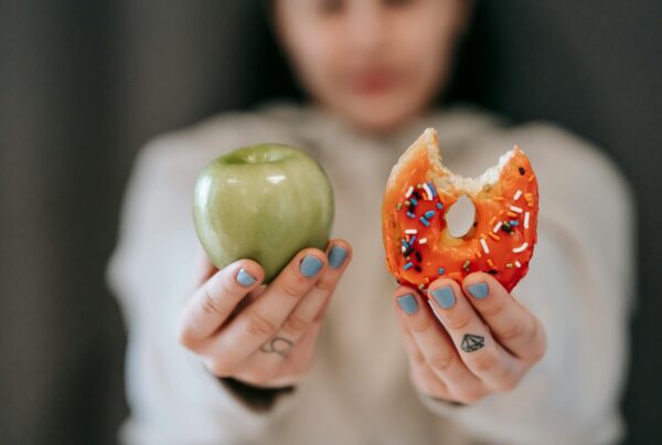 Child holding a green apple in right hand and sprinkle-covered donut in left hand.