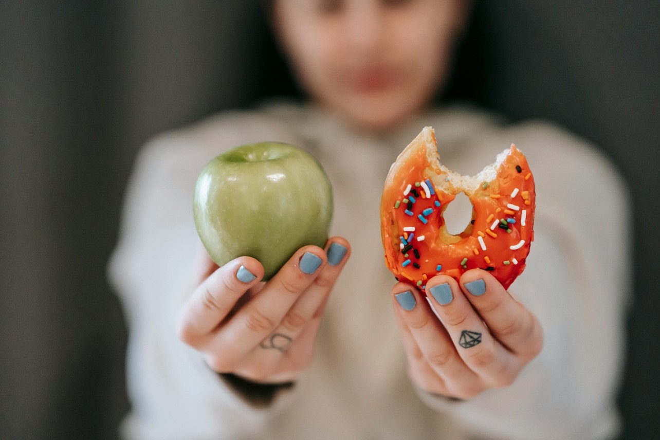 Child holding a green apple in right hand and sprinkle-covered donut in left hand.