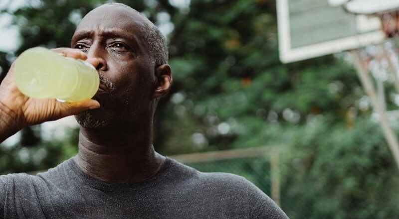 African American male holding a basketball drinking an energy drink or electrolyte replacement