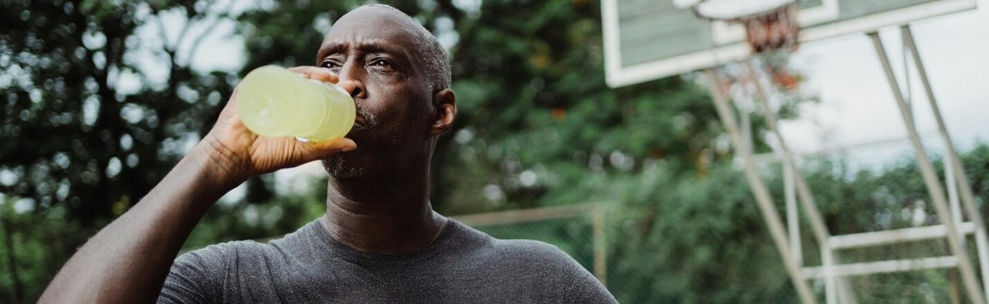 African American male holding a basketball drinking an energy drink or electrolyte replacement