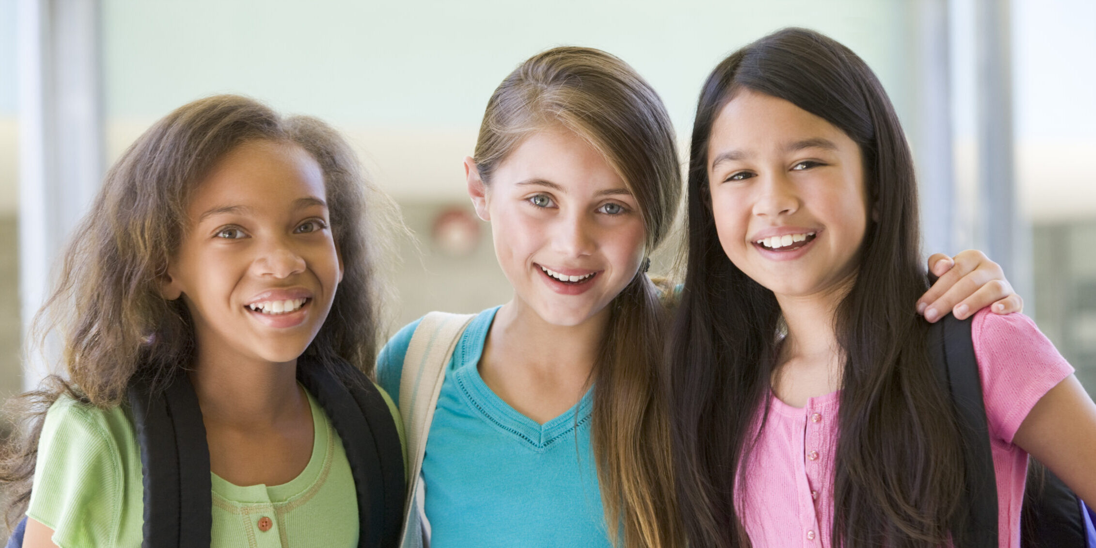 A group of female elementary school friends smiling in the hallway with their arms around each other