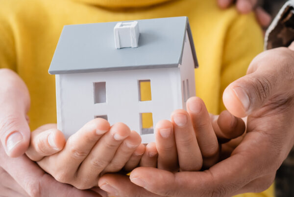 Cropped view of parents in military uniform holding model of house with daughter, banner