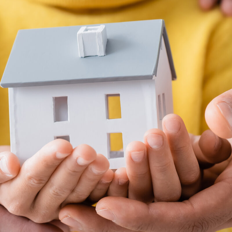 Cropped view of parents in military uniform holding model of house with daughter, banner