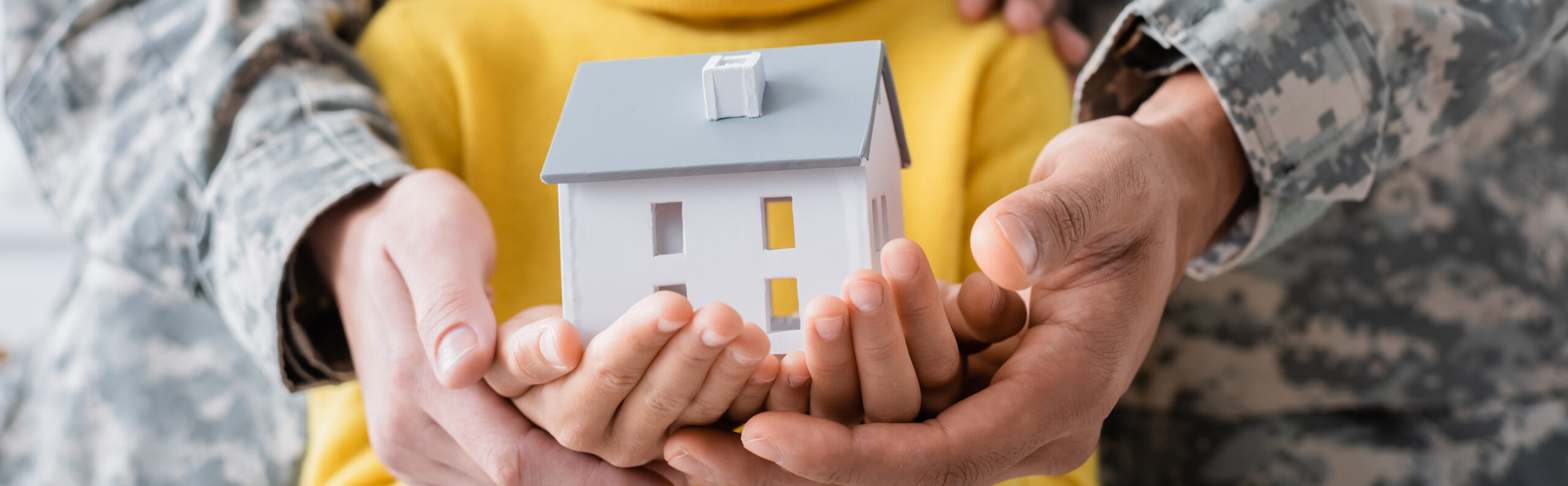 Cropped view of parents in military uniform holding model of house with daughter, banner