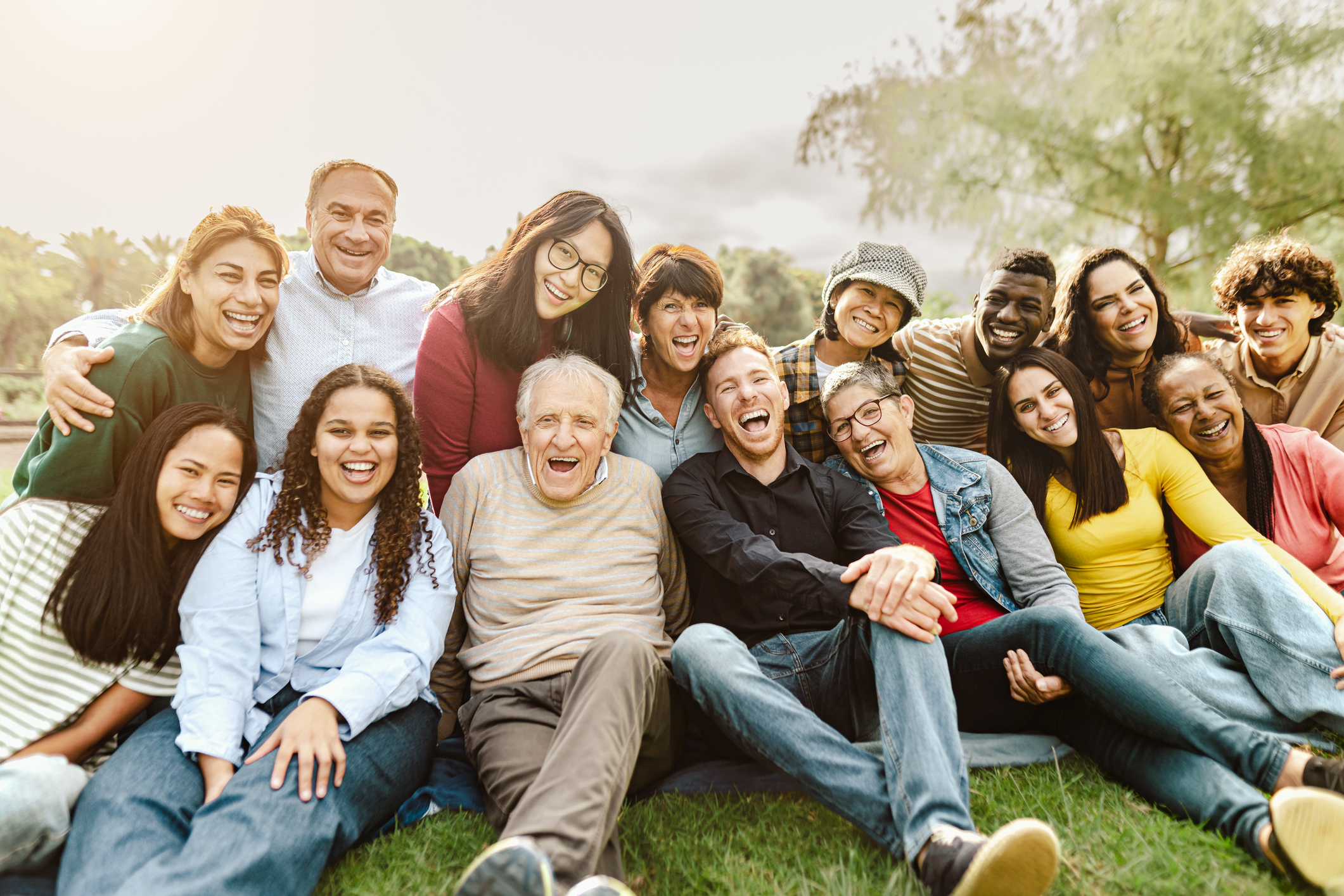 Happy multigenerational people having fun sitting on grass in a public park