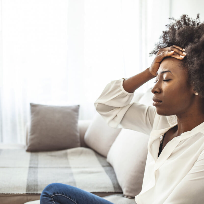 Lonely sad woman deep in thoughts sitting daydreaming or waiting for someone in the living room with a serious expression, she is pensive and suffering from insomnia sitting on couch