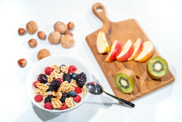 Breakfast bowl with raspberries, blueberries, blackberries and walnuts. Cutting board with sliced apple and kiwi.