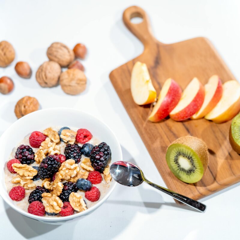 Breakfast bowl with raspberries, blueberries, blackberries and walnuts. Cutting board with sliced apple and kiwi.