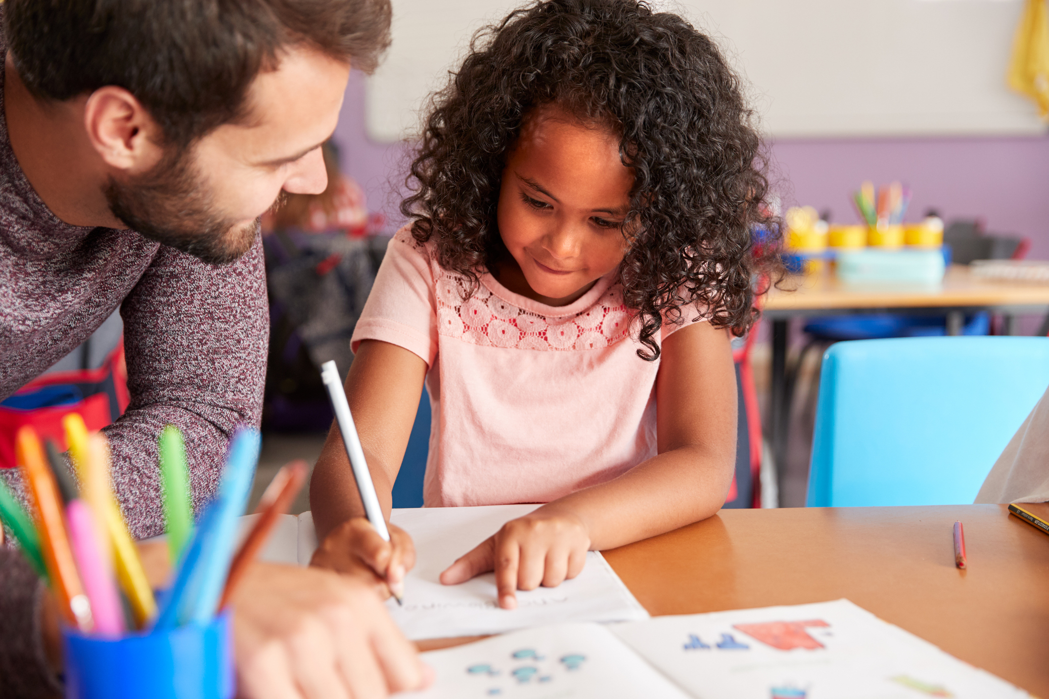 Elementary School Teacher Giving Female Pupil One To One Support In Classroom