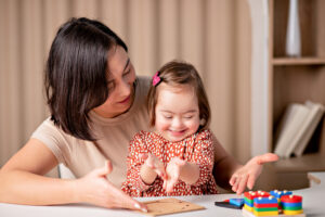 child with down syndrome with educational toys smiles, a cute girl with her mother a teacher