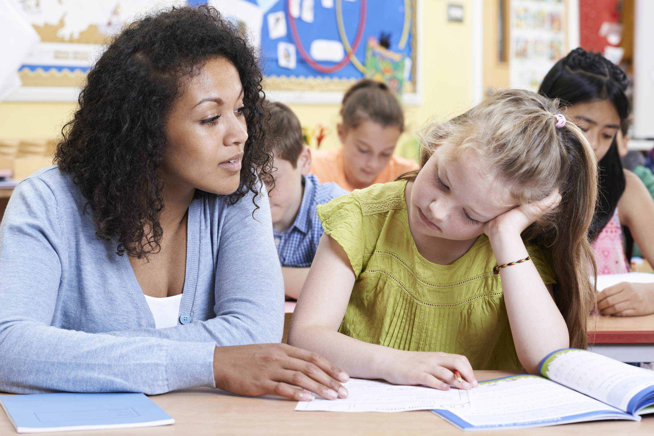 Elementary School Teacher Giving Female Pupil One To One Support In Classroom