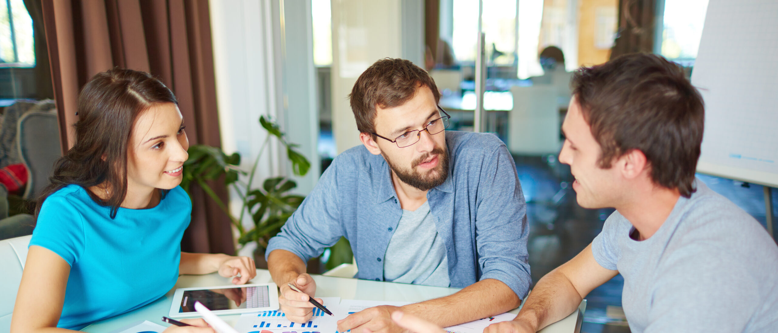 Group of three successful business partners in casual discussing ideas at meeting in office
