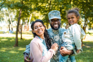 Black man in military uniform holding preschool aged girl and embracing his female partner all smiling happily for the camera