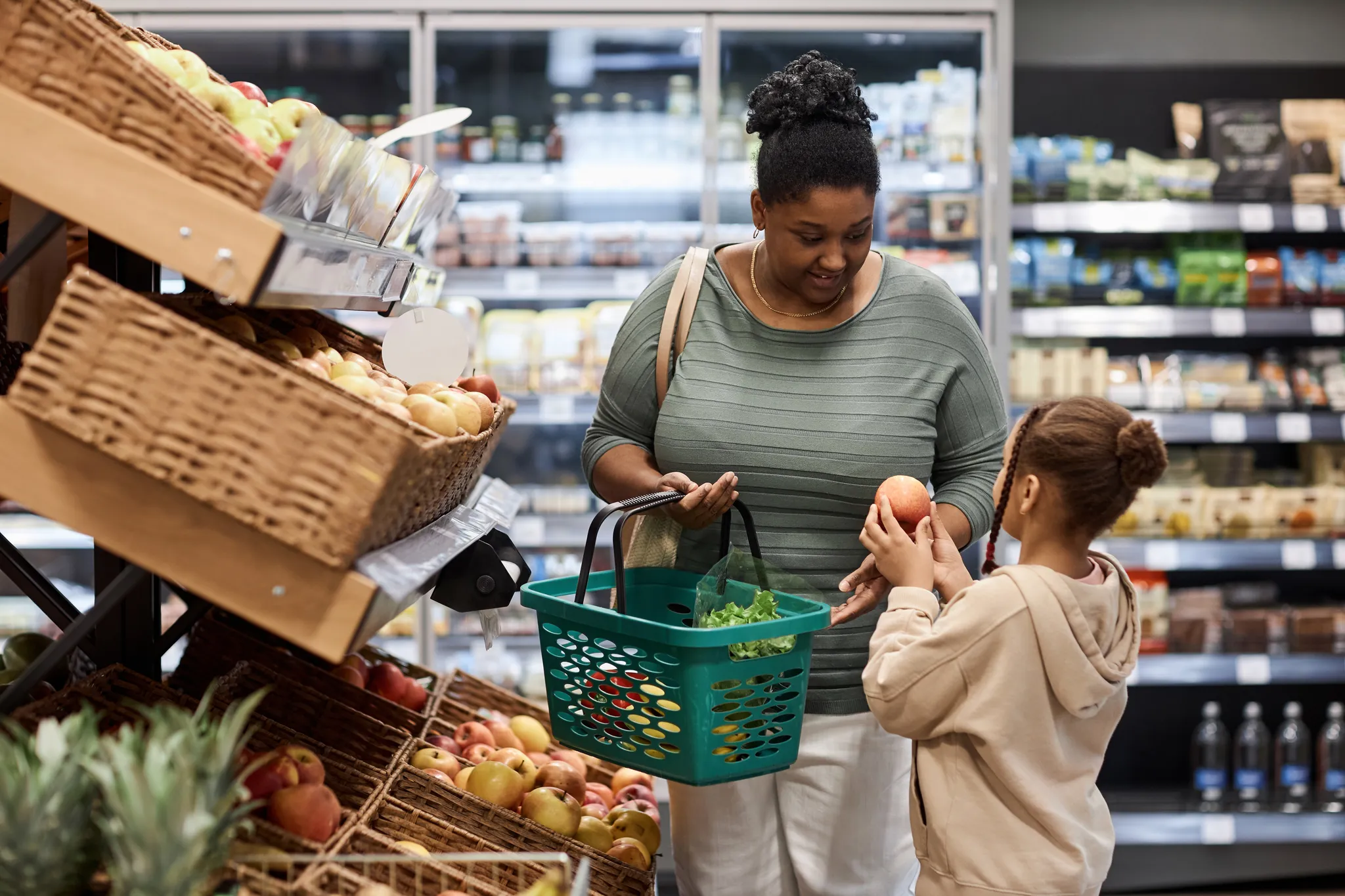 Portrait of real black woman shopping in supermarket with little daughter and buying fresh vegetables