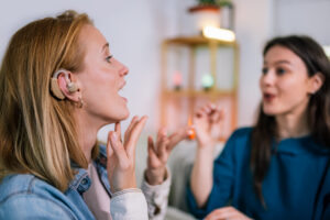 Two women communicating in sign language, one wearing a hearing aid