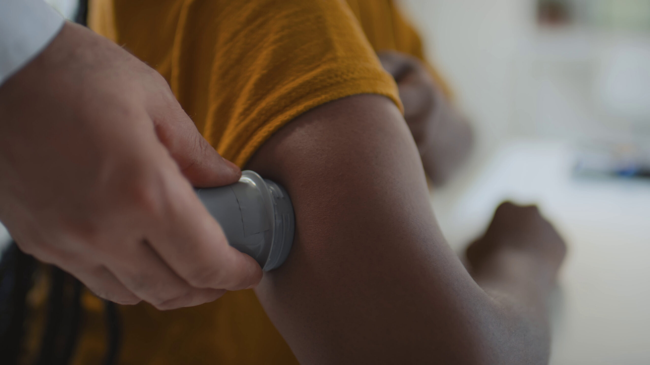 Close up shot of hands of unrecognizable medical practitioner implanting continuous glucose monitor on upper arm.