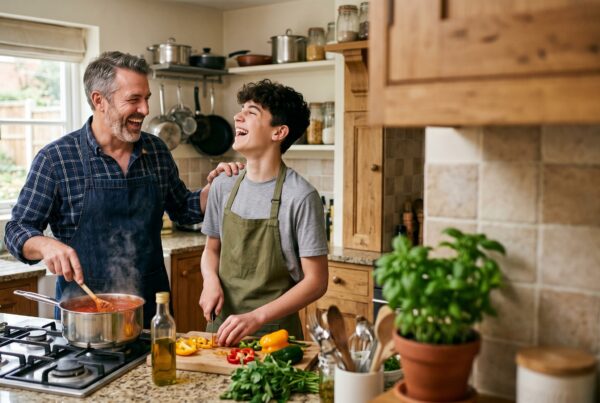 Father and son laughing while cooking together in a bright, modern kitchen preparing a healthy meal with fresh ingredients