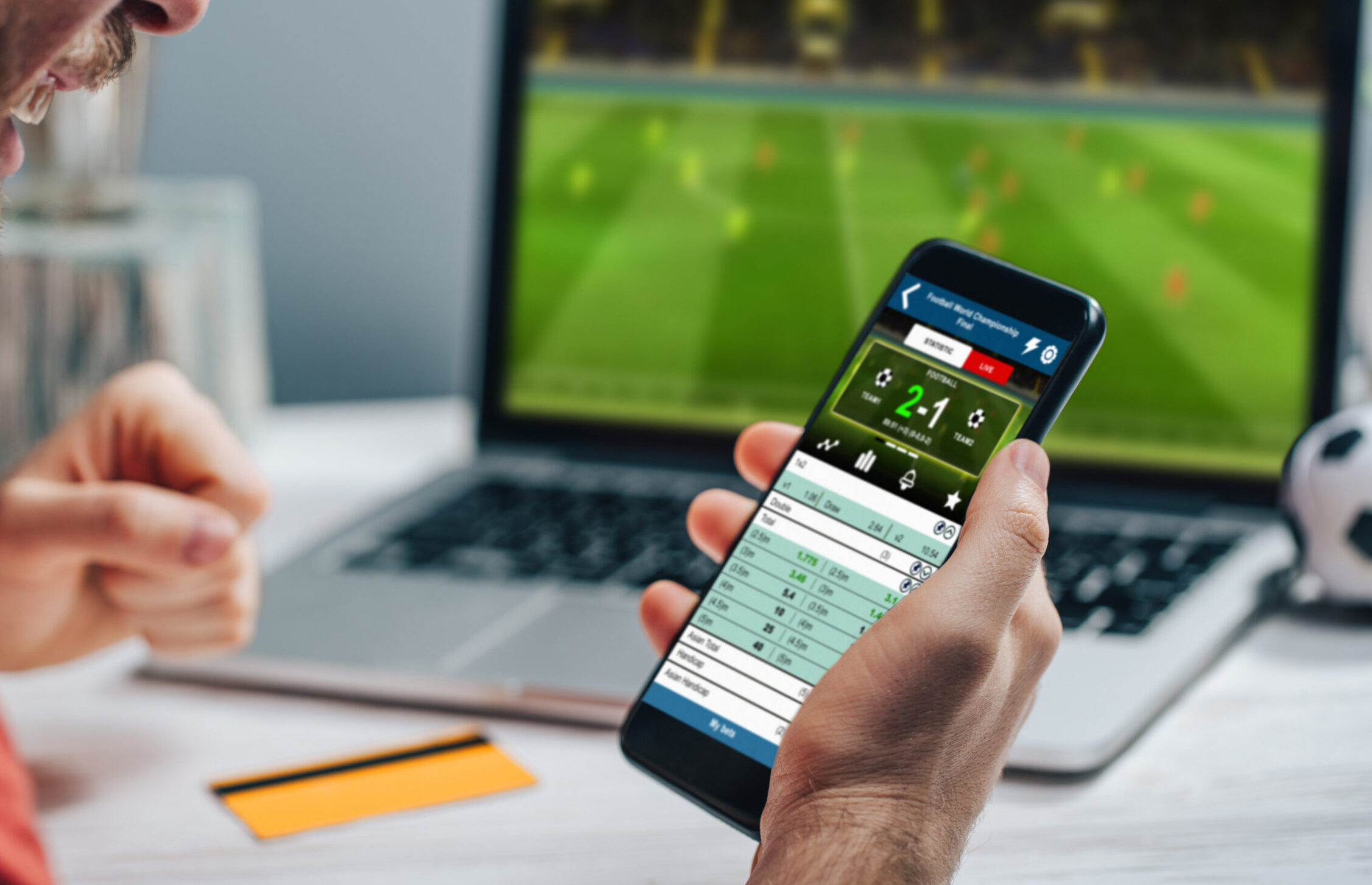 Young bearded man showing sincere excitement about his favorite team victory. Guy being happy winning a bet in online sport gambling application on his mobile phone.