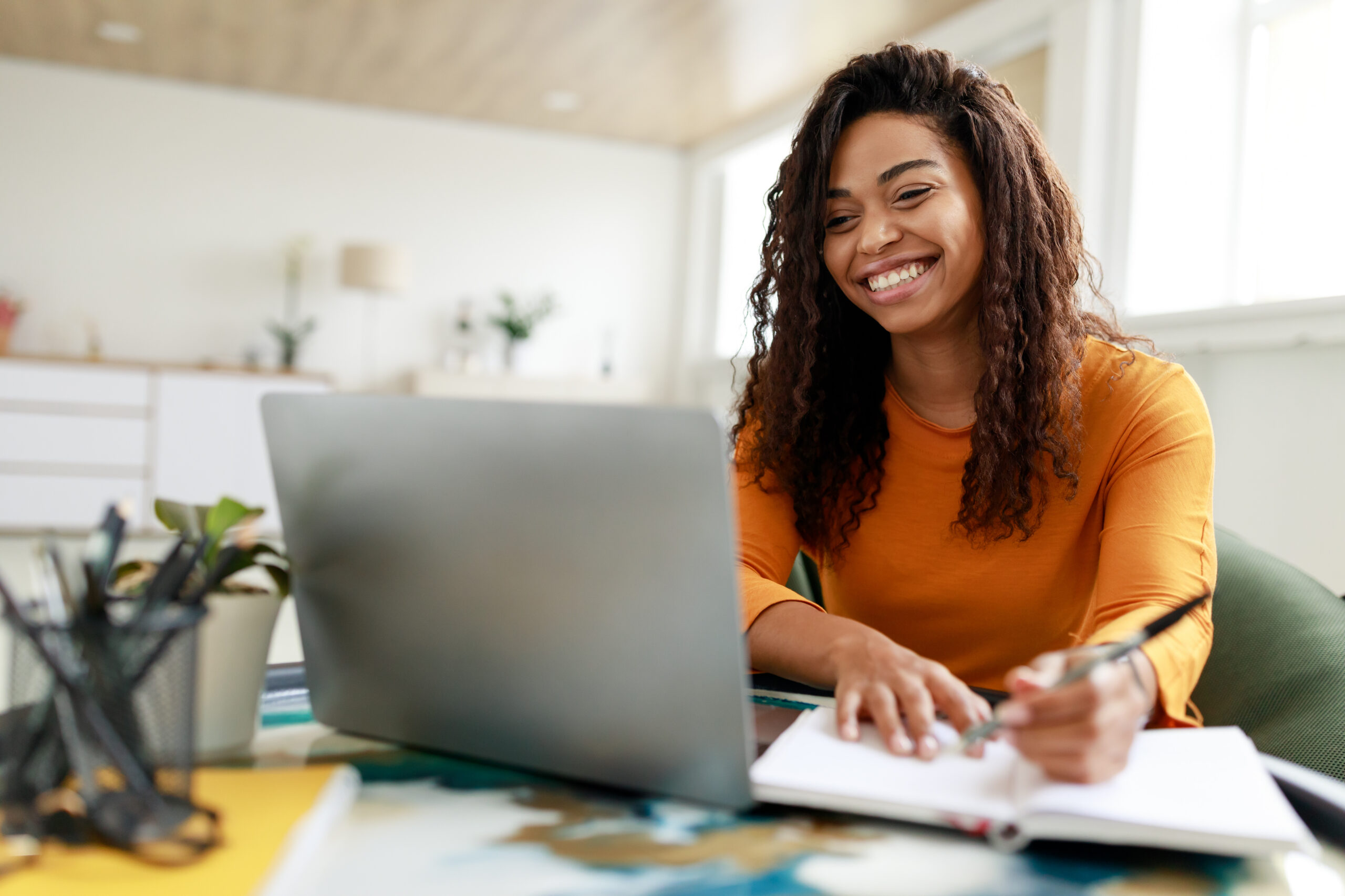 smiling woman taking notes at a laptop